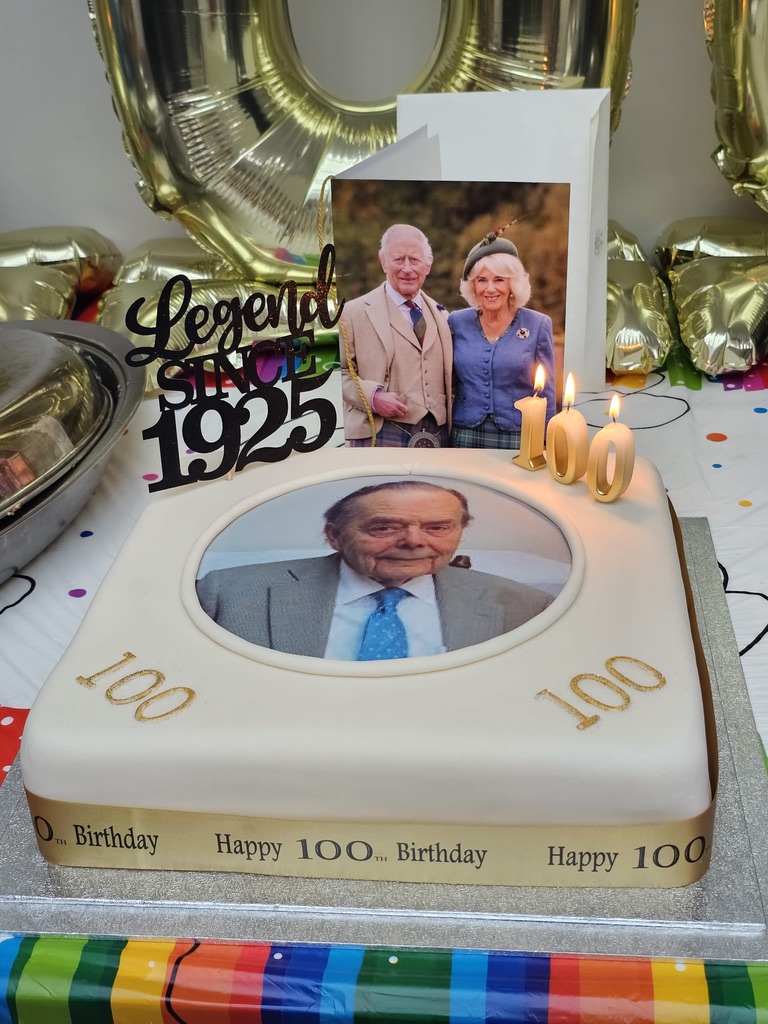 John's 100th birthday cake with his photograph, a “Legend since 1925” topper and a birthday card from the King and Queen