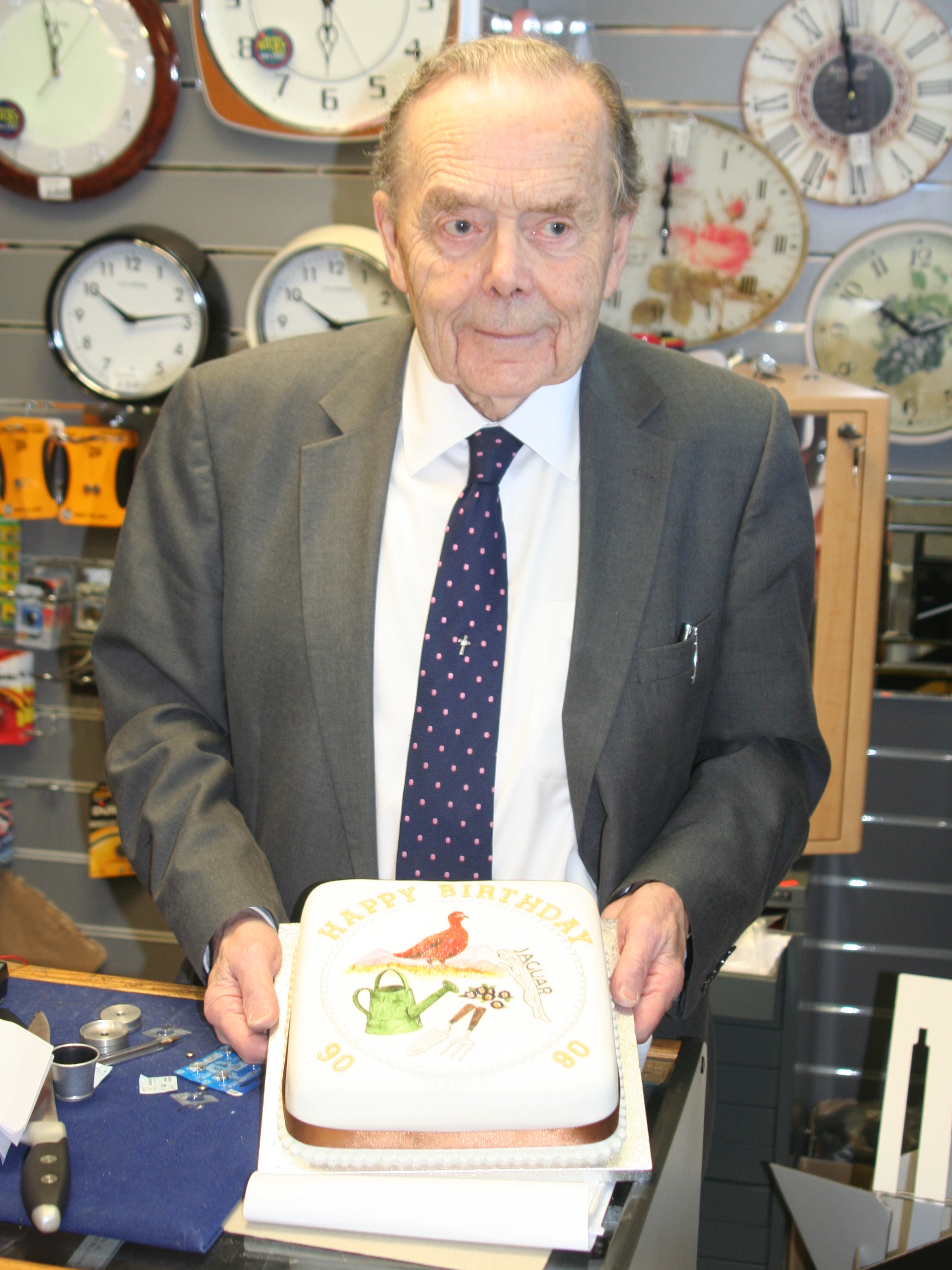 John Brown behind the shop counter holding his 90th birthday cake
